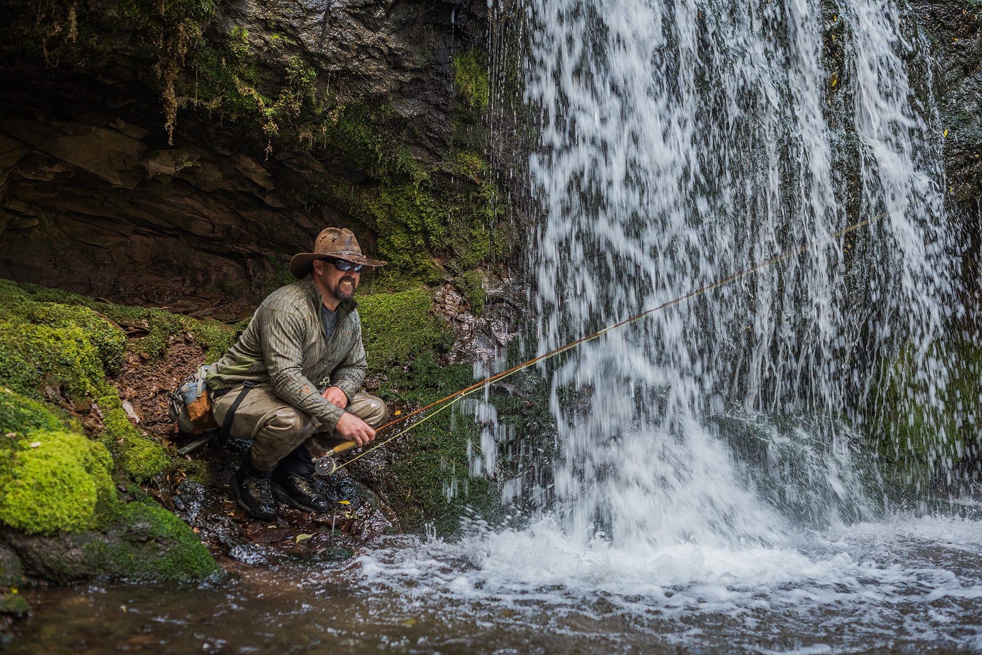 PJ by a waterfall with a bamboo rod.