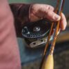 Hand holding a reel and bamboo fly rod.