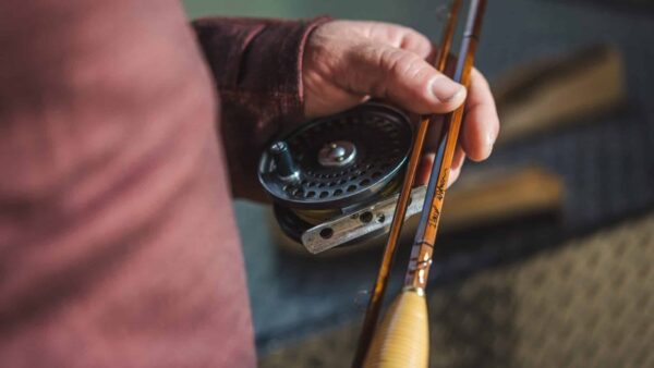 Hand holding a reel and bamboo fly rod.