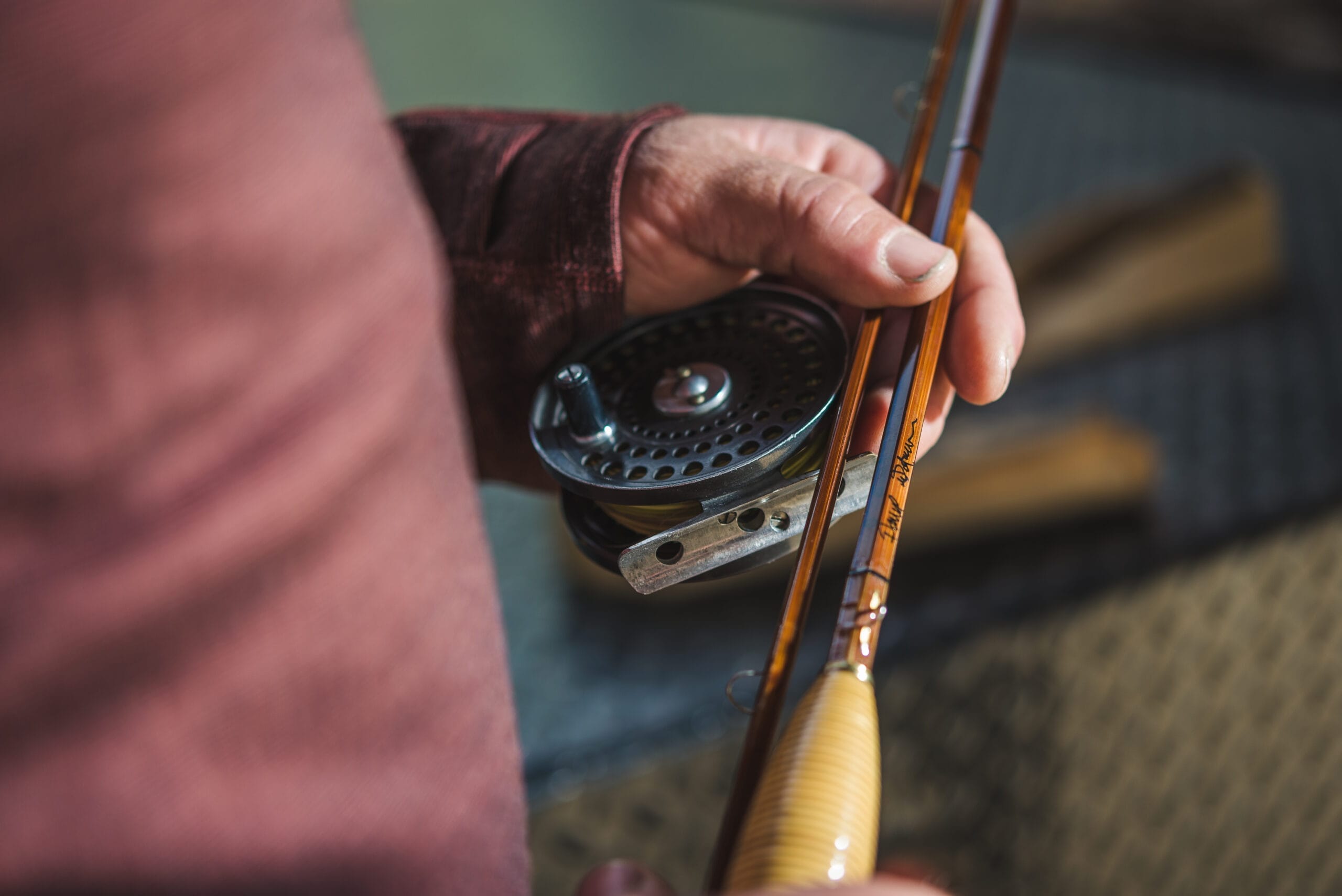 Hand holding a reel and bamboo fly rod.